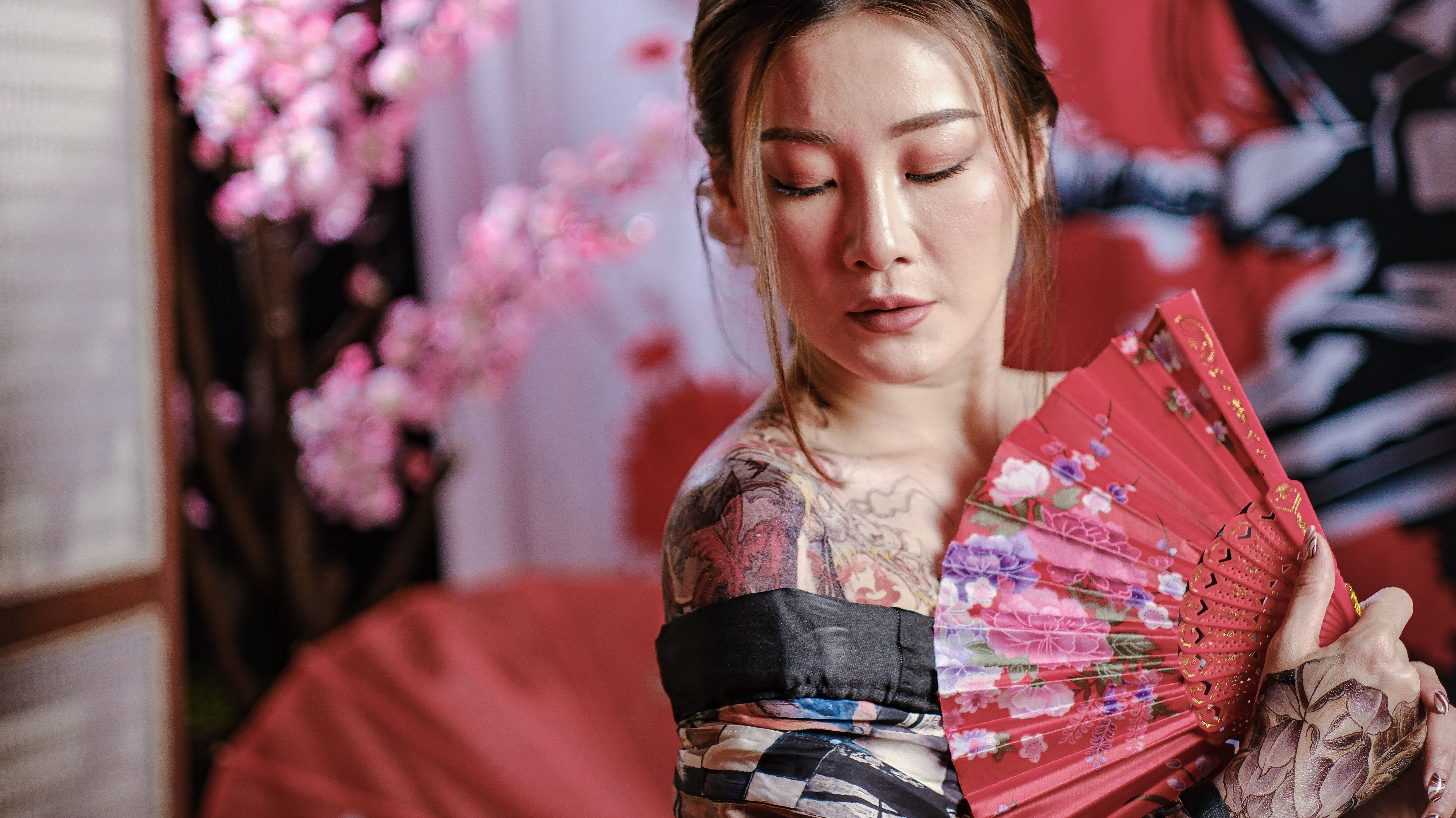 Mulher com kimono e tatuagem japonesa no ombro segurando leque vermelho